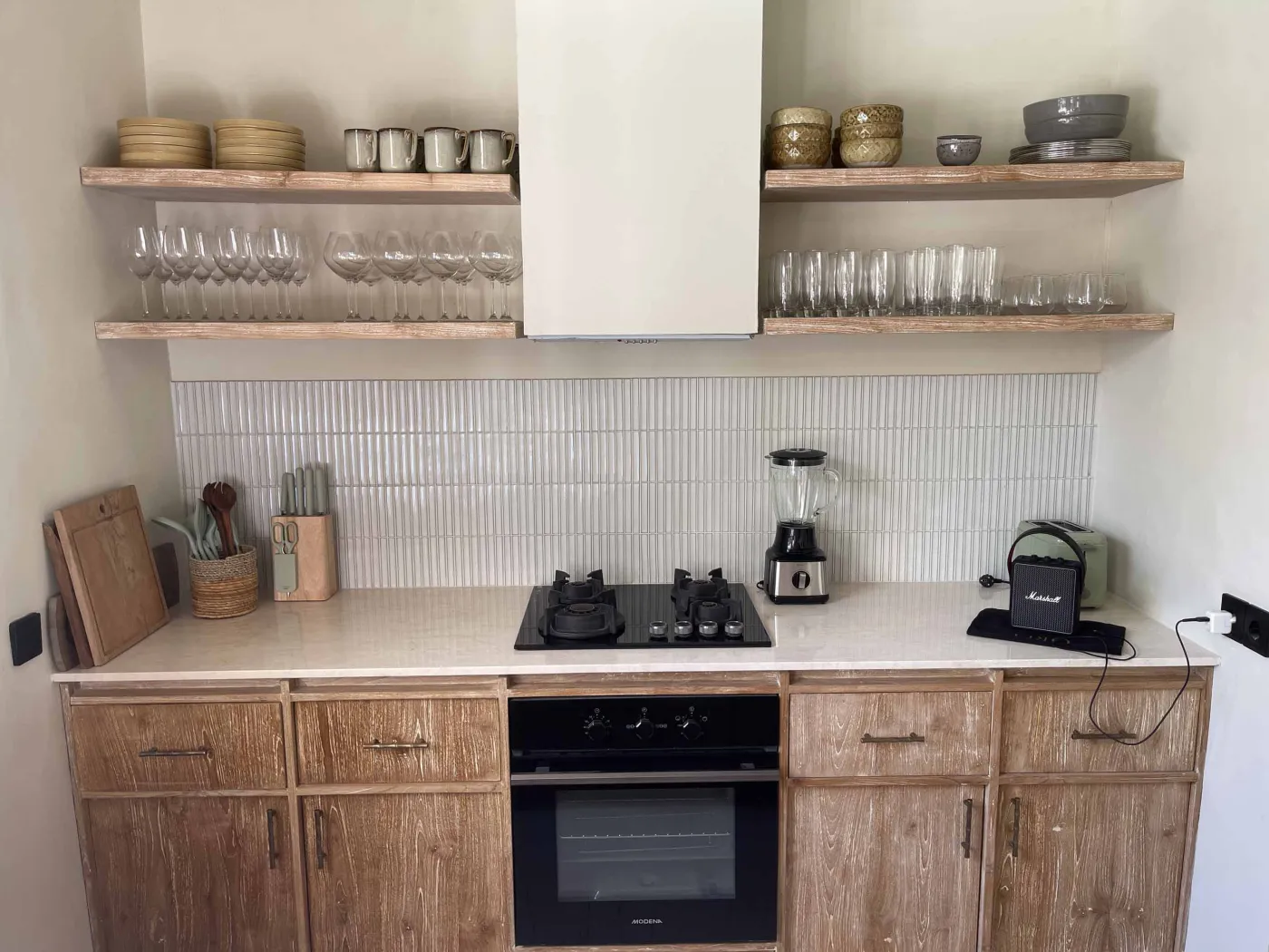 Cozy Balinese-style lounge with arched niche walls displaying pottery and sculptures, gray L-shaped sofa with patterned pillows, wooden trunk coffee table, and large window. - Bali Villas