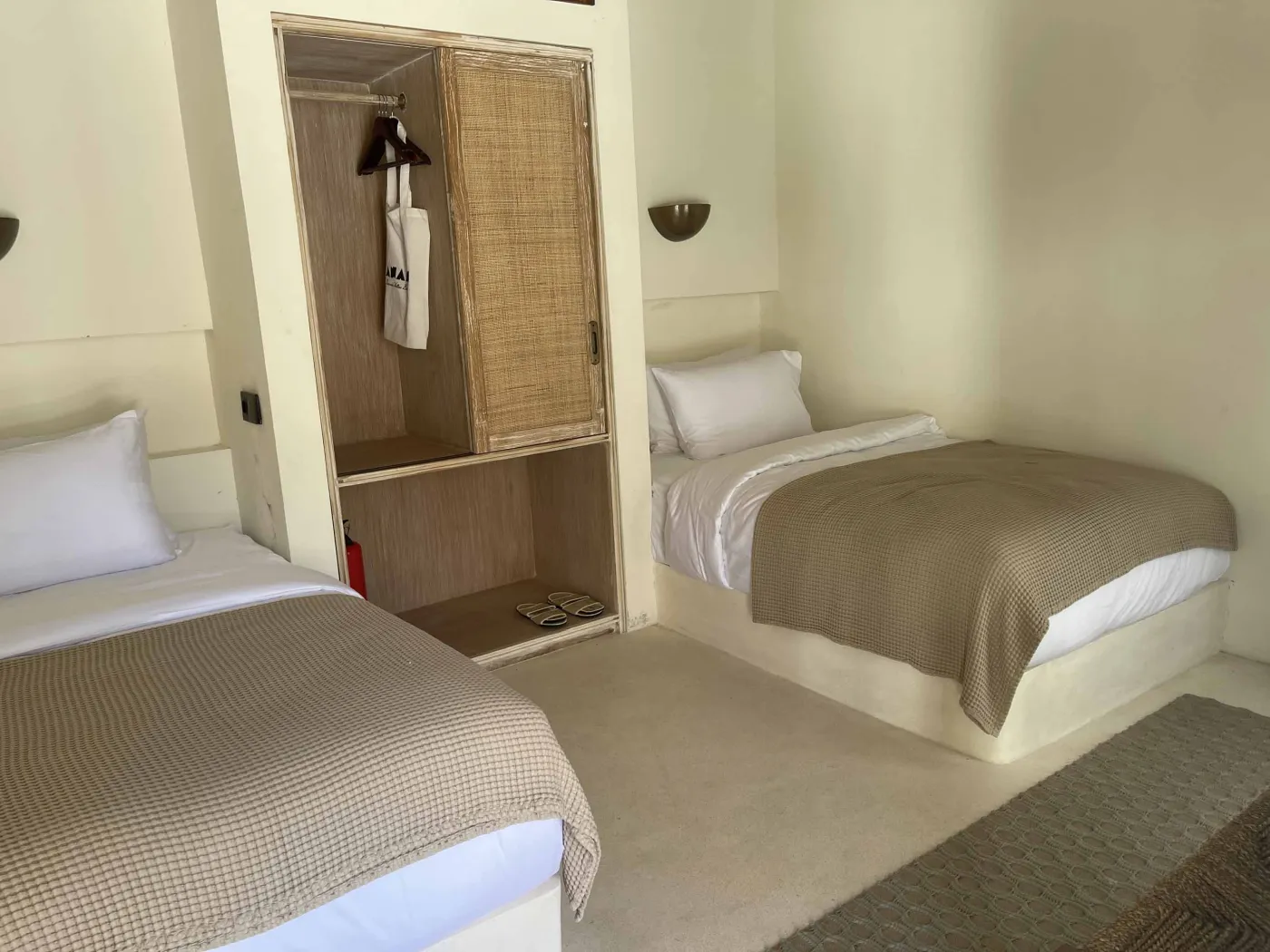 Cozy Balinese-style lounge with arched niche walls displaying pottery and sculptures, gray L-shaped sofa with patterned pillows, wooden trunk coffee table, and large window. - Bali Villas