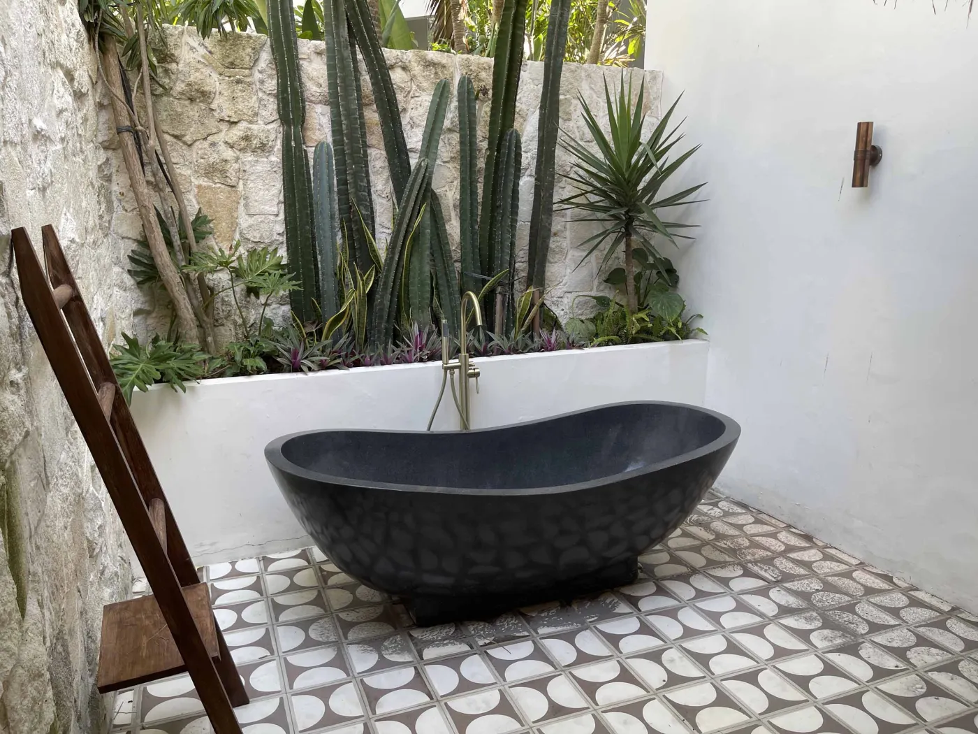 Cozy Balinese-style lounge with arched niche walls displaying pottery and sculptures, gray L-shaped sofa with patterned pillows, wooden trunk coffee table, and large window. - Bali Villas