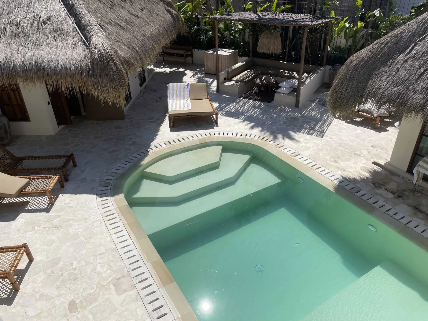 Cozy Balinese-style lounge with arched niche walls displaying pottery and sculptures, gray L-shaped sofa with patterned pillows, wooden trunk coffee table, and large window. - Bali Villas