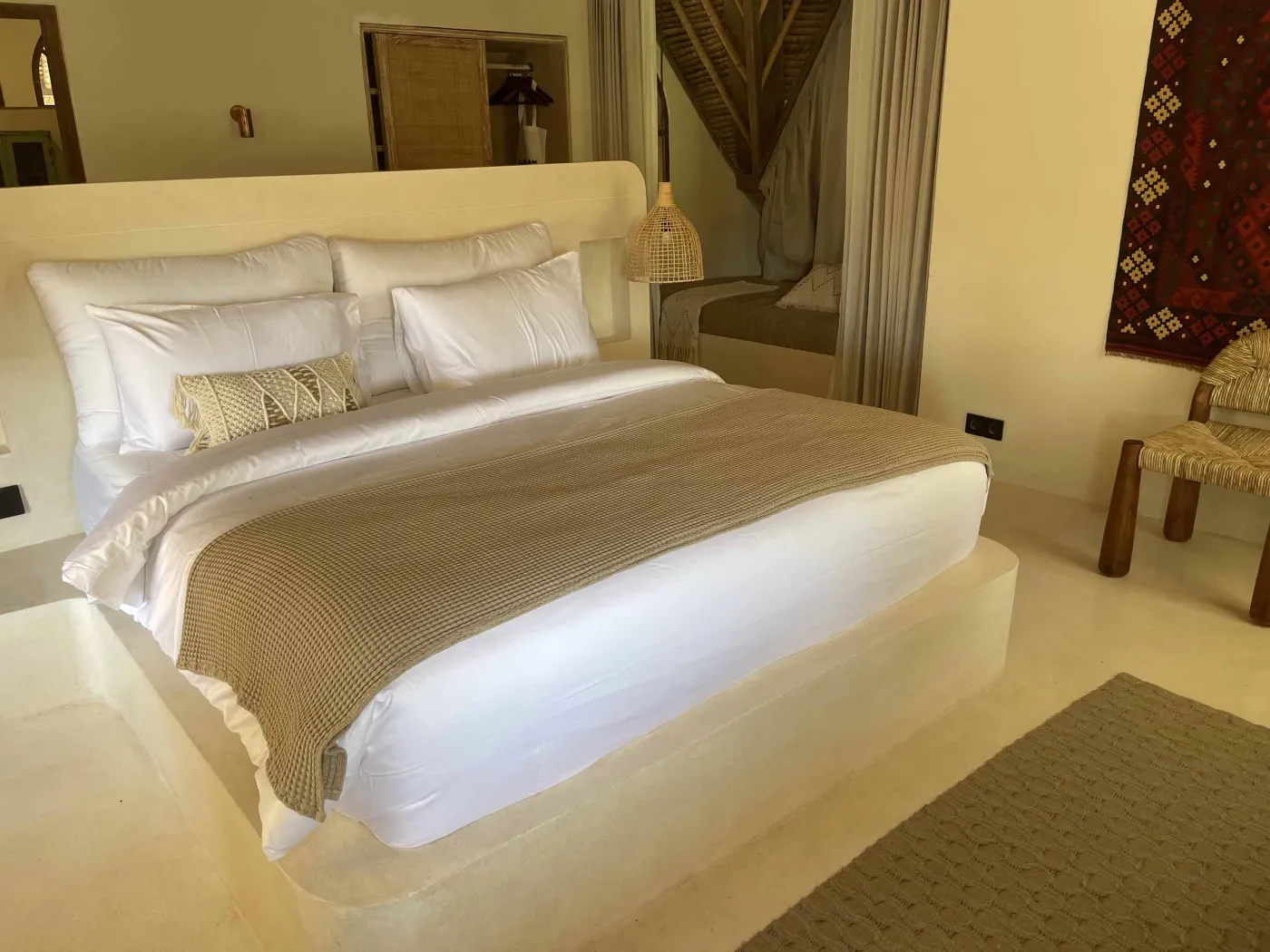 Cozy Balinese-style lounge with arched niche walls displaying pottery and sculptures, gray L-shaped sofa with patterned pillows, wooden trunk coffee table, and large window. - Bali Villas