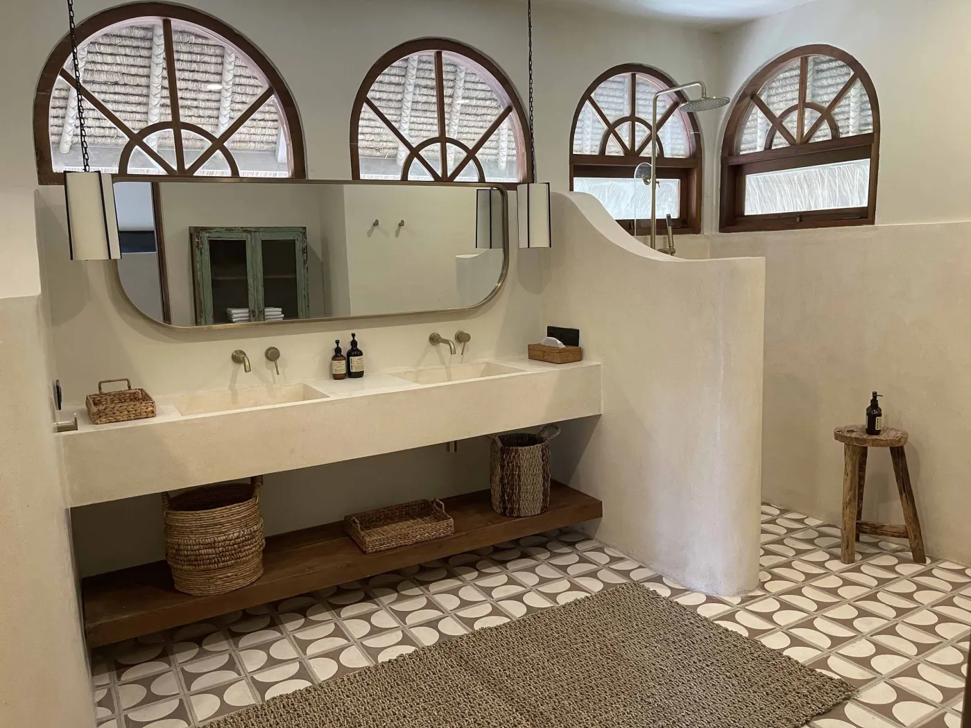 Cozy Balinese-style lounge with arched niche walls displaying pottery and sculptures, gray L-shaped sofa with patterned pillows, wooden trunk coffee table, and large window. - Bali Villas