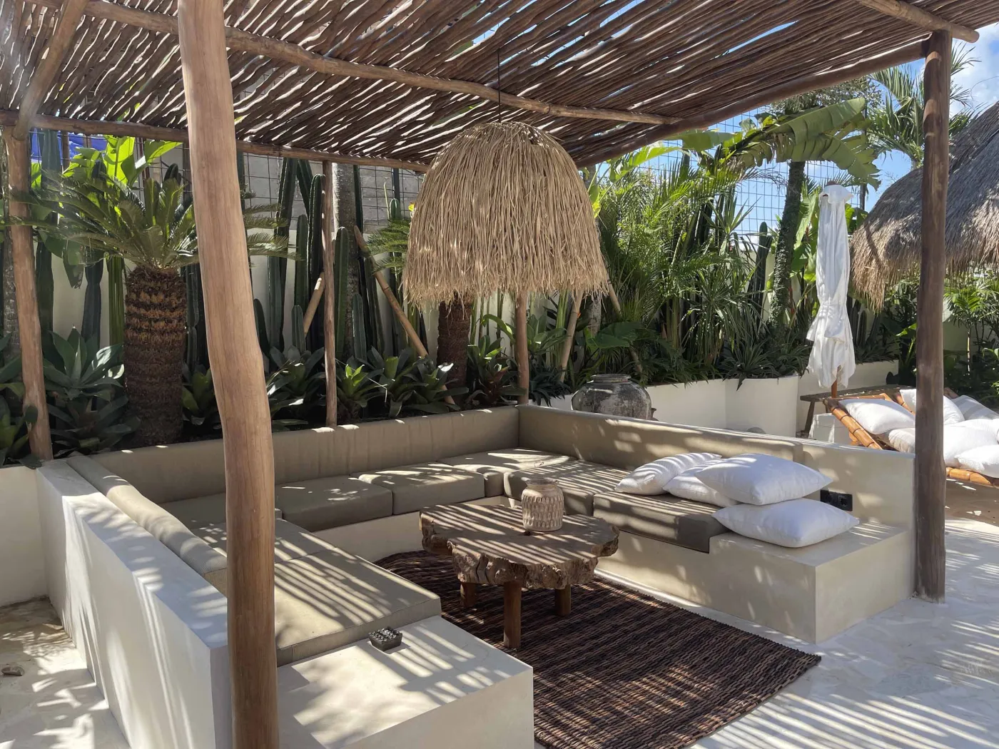 Cozy Balinese-style lounge with arched niche walls displaying pottery and sculptures, gray L-shaped sofa with patterned pillows, wooden trunk coffee table, and large window. - Bali Villas