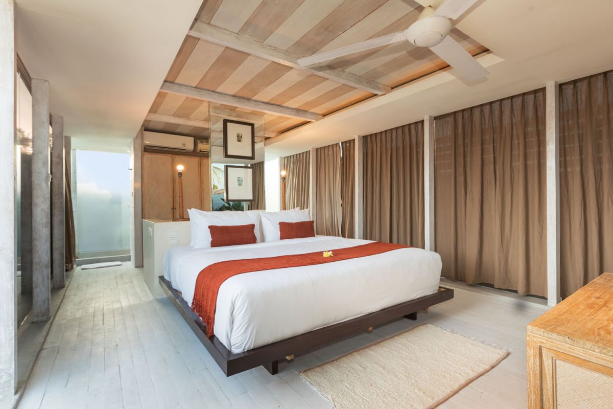 Spacious modern tropical villa interior with wooden furniture, lush plants, and open views to a pool. - Bali Villas