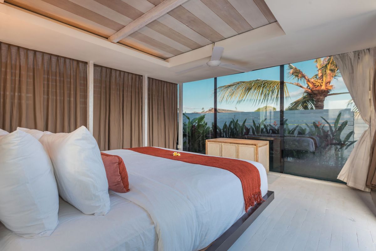 Spacious modern tropical villa interior with wooden furniture, lush plants, and open views to a pool. - Bali Villas