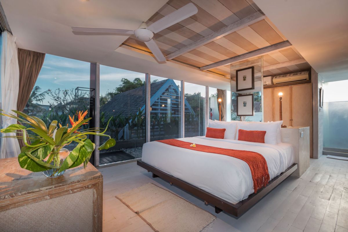 Spacious modern tropical villa interior with wooden furniture, lush plants, and open views to a pool. - Bali Villas