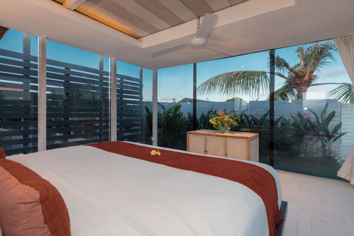 Spacious modern tropical villa interior with wooden furniture, lush plants, and open views to a pool. - Bali Villas