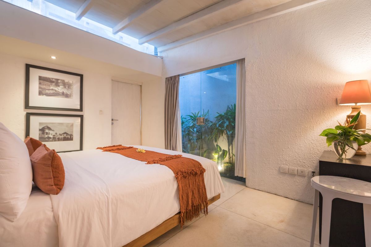 Spacious modern tropical villa interior with wooden furniture, lush plants, and open views to a pool. - Bali Villas