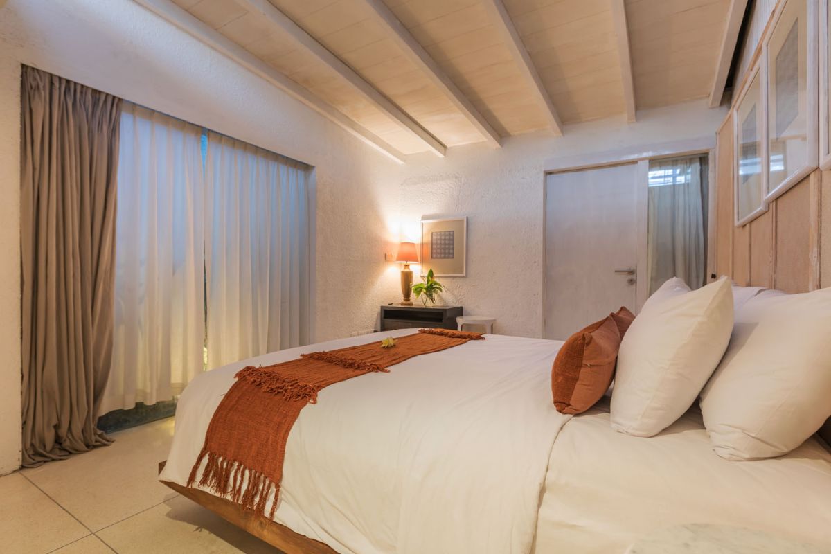 Spacious modern tropical villa interior with wooden furniture, lush plants, and open views to a pool. - Bali Villas