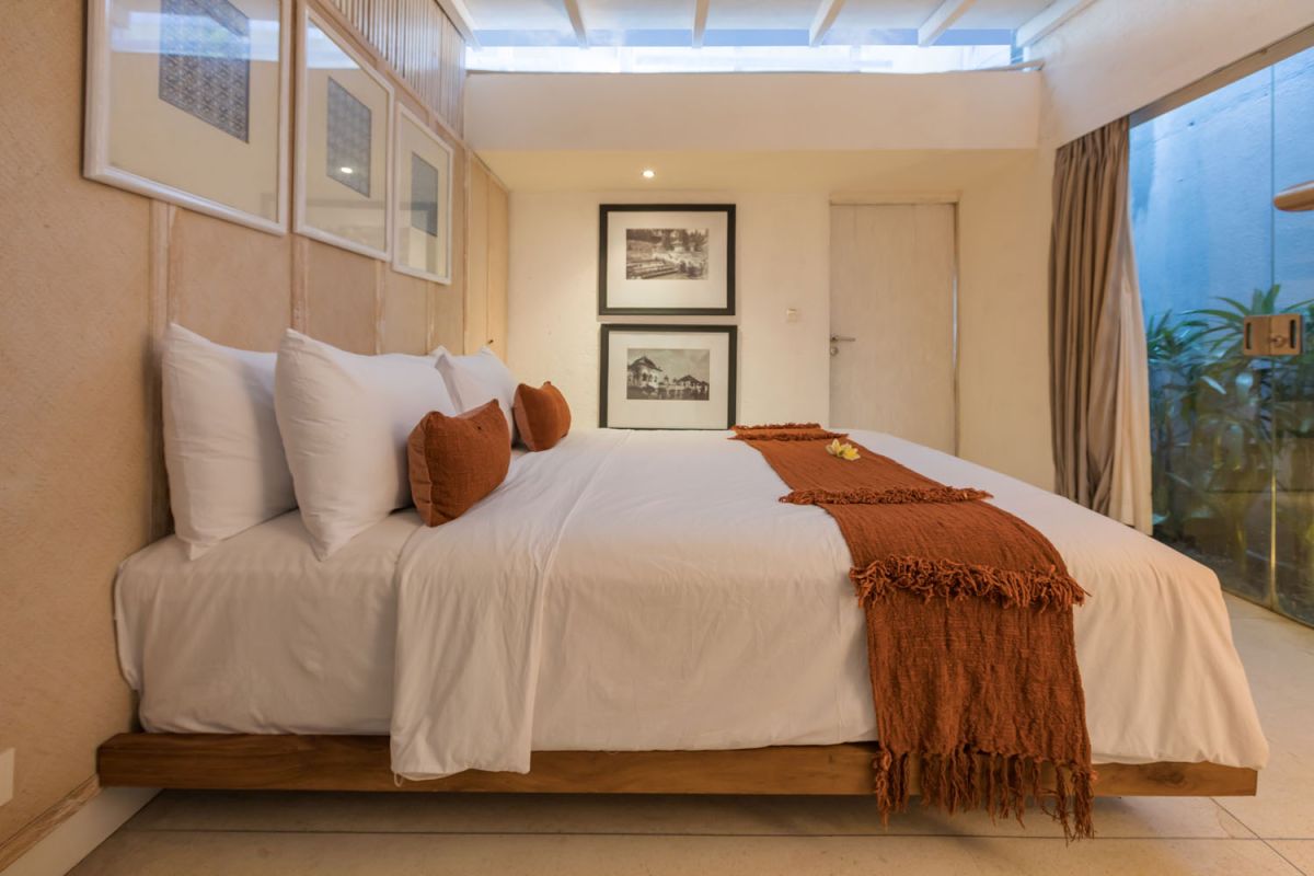 Spacious modern tropical villa interior with wooden furniture, lush plants, and open views to a pool. - Bali Villas