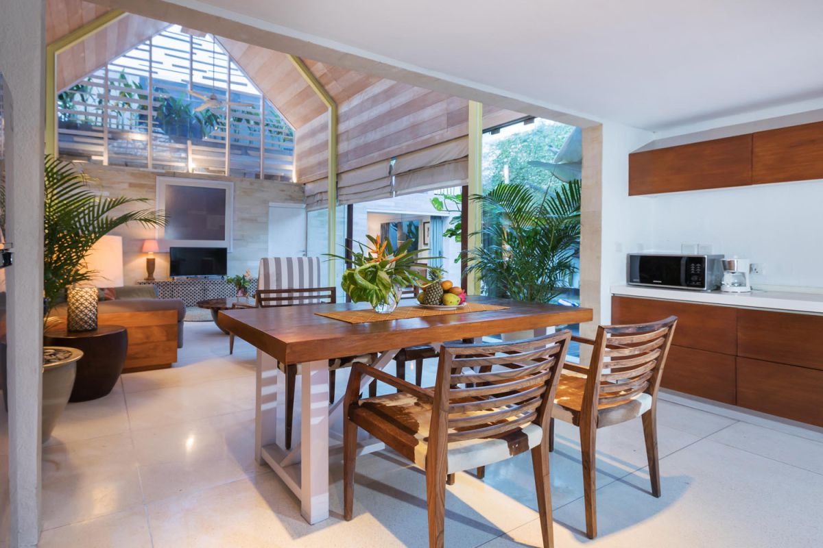 Spacious modern tropical villa interior with wooden furniture, lush plants, and open views to a pool. - Bali Villas