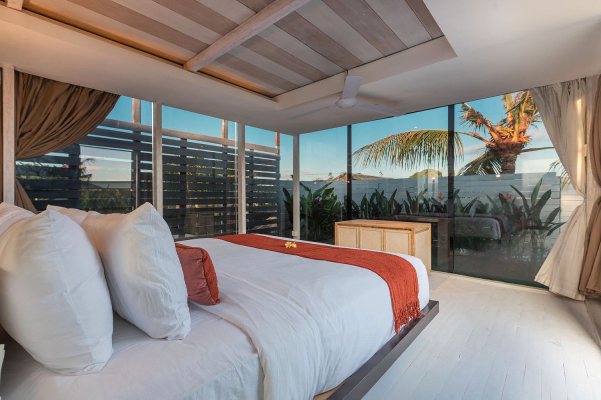 Spacious modern tropical villa interior with wooden furniture, lush plants, and open views to a pool. - Bali Villas