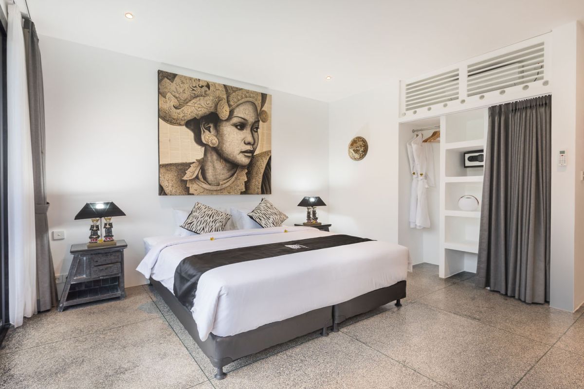 Spacious modern Bali villa interior featuring a purple modular sofa, abstract African-inspired wall art, wooden dining table, and polished concrete floors. - Bali Villas