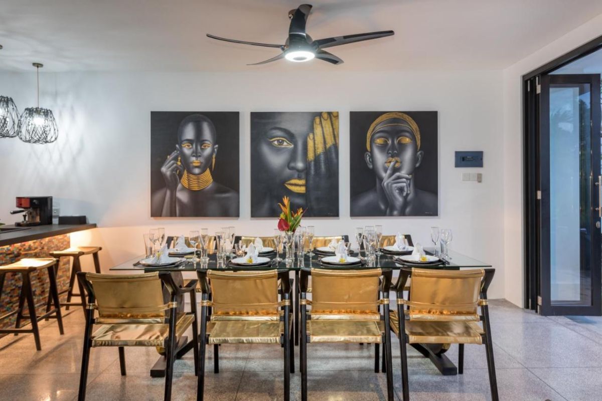 Spacious modern Bali villa interior featuring a purple modular sofa, abstract African-inspired wall art, wooden dining table, and polished concrete floors. - Bali Villas