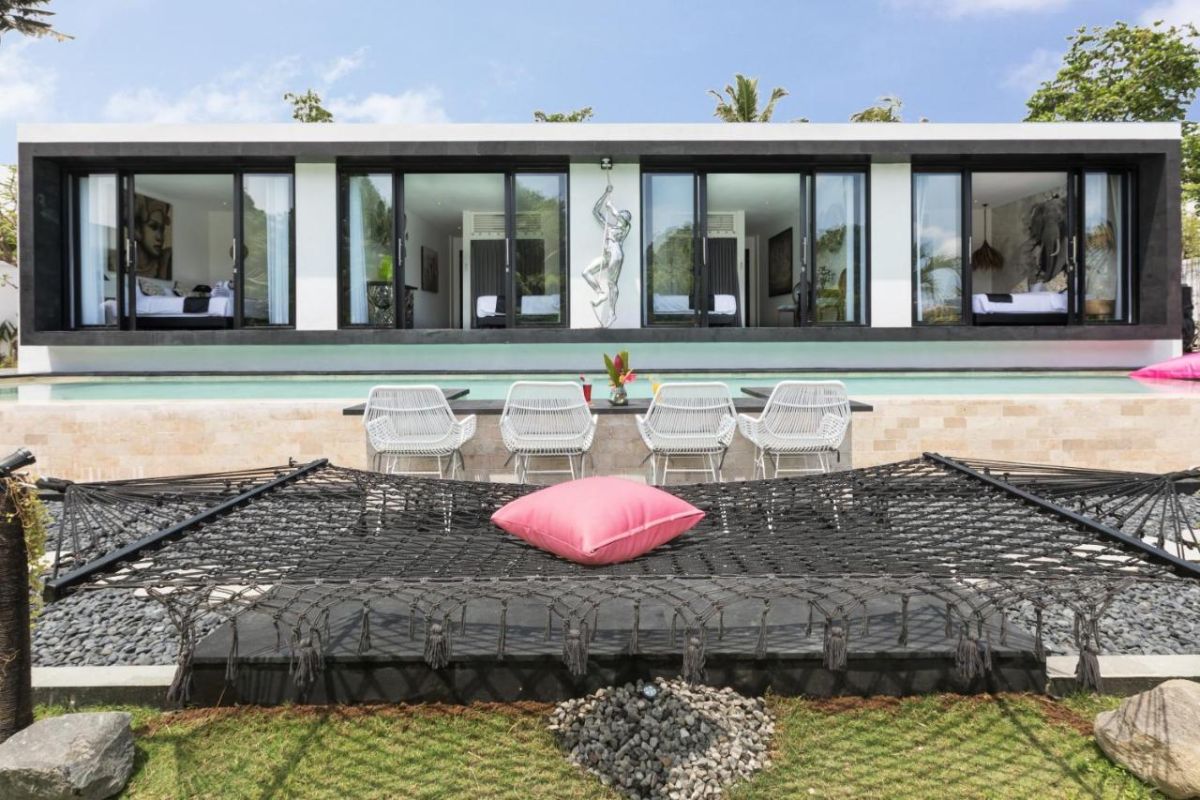 Spacious modern Bali villa interior featuring a purple modular sofa, abstract African-inspired wall art, wooden dining table, and polished concrete floors. - Bali Villas