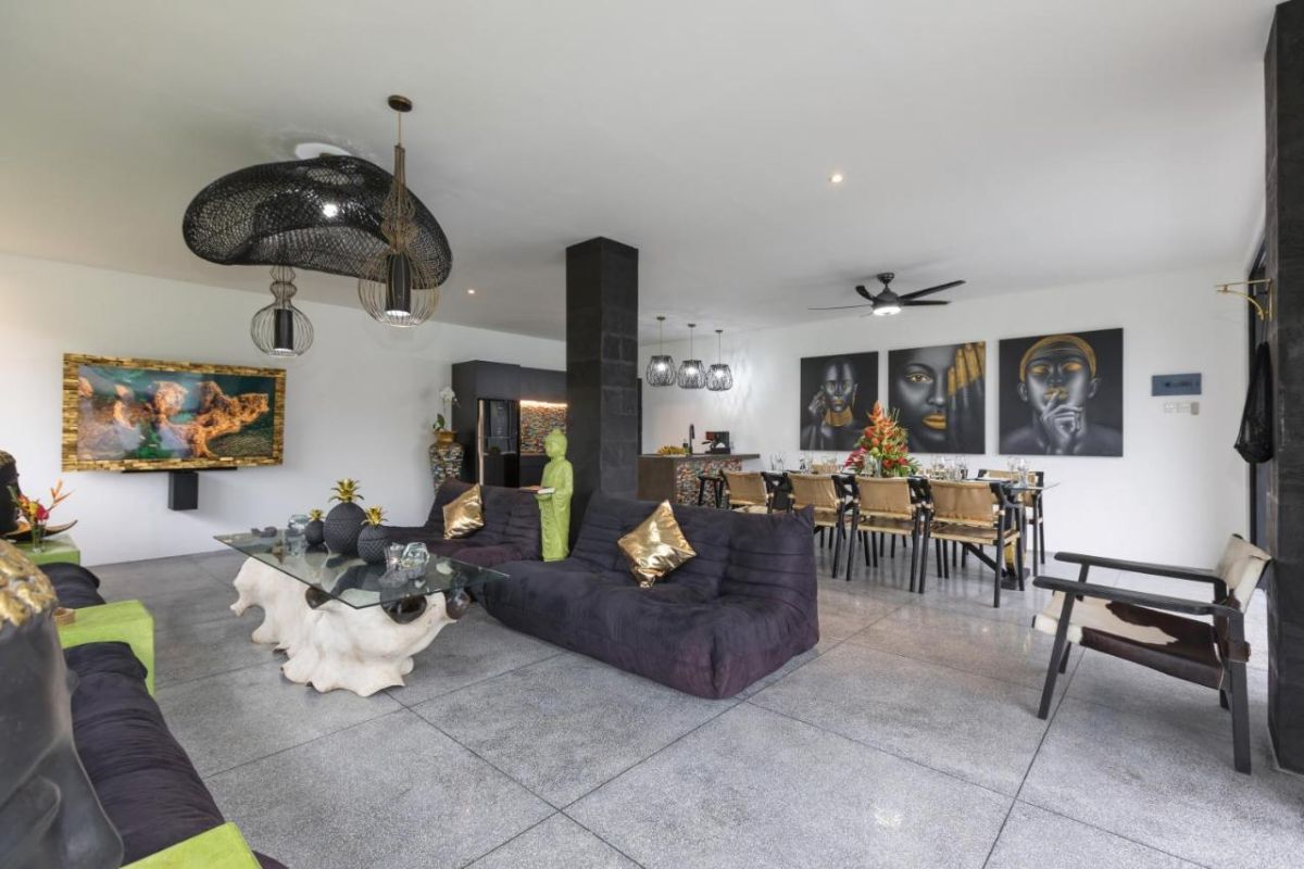 Spacious modern Bali villa interior featuring a purple modular sofa, abstract African-inspired wall art, wooden dining table, and polished concrete floors. - Bali Villas
