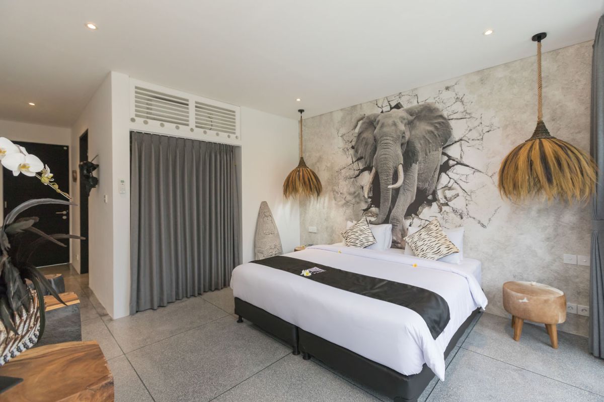 Spacious modern Bali villa interior featuring a purple modular sofa, abstract African-inspired wall art, wooden dining table, and polished concrete floors. - Bali Villas