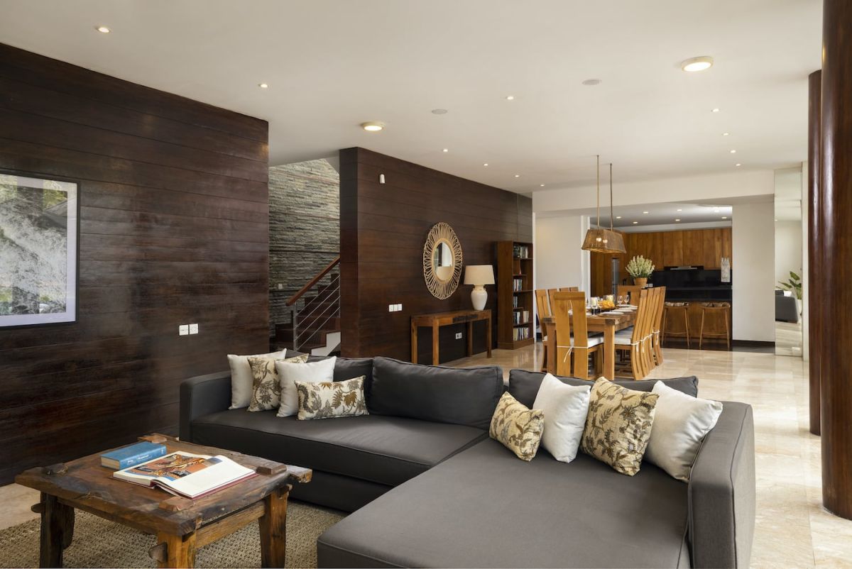 Spacious Bali villa bedroom with wooden floors, king bed, desk, lounge seating, and tropical garden views through large glass doors. - Bali Villas