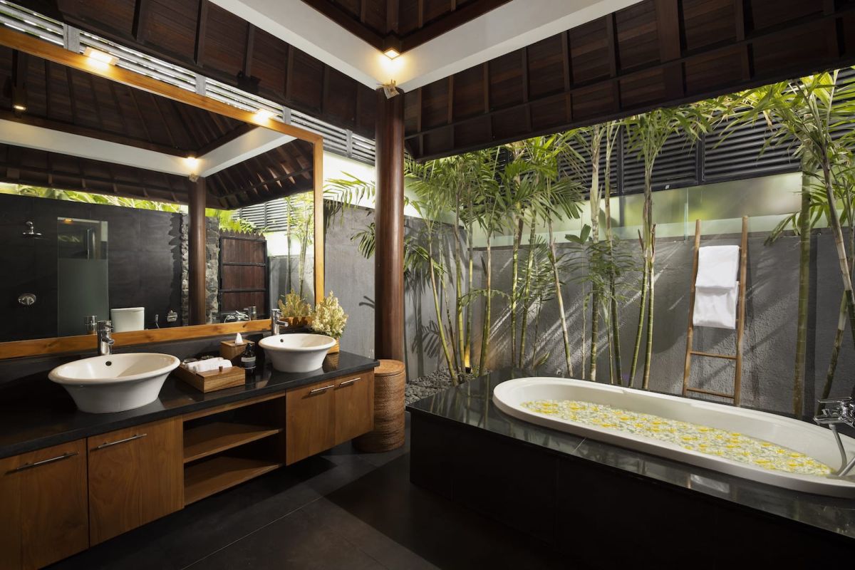 Spacious Bali villa bedroom with wooden floors, king bed, desk, lounge seating, and tropical garden views through large glass doors. - Bali Villas