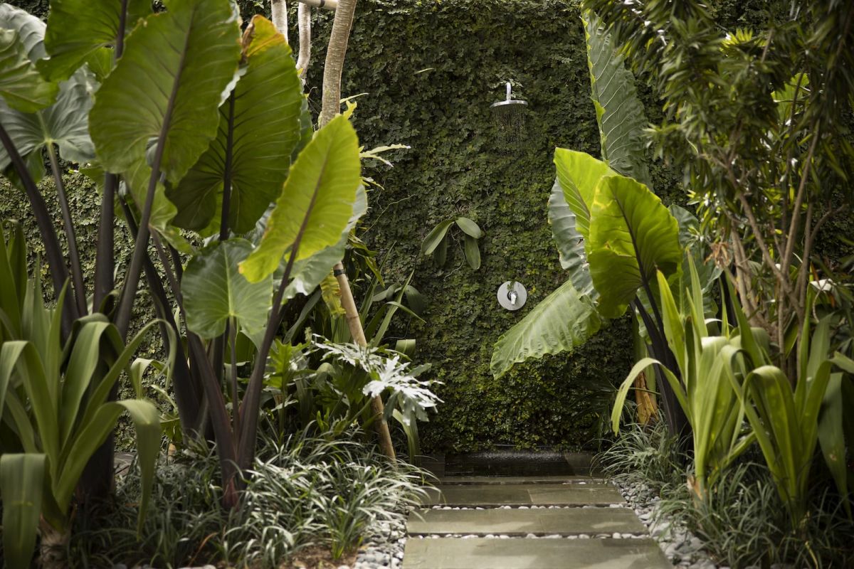 Spacious Bali villa bedroom with wooden floors, king bed, desk, lounge seating, and tropical garden views through large glass doors. - Bali Villas