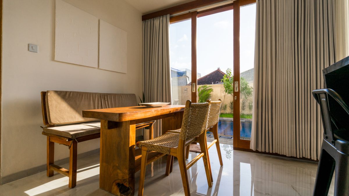Serene Bali villa poolside patio with wooden dining set under blue umbrella, surrounded by tropical plants and traditional architecture. - Bali Villas