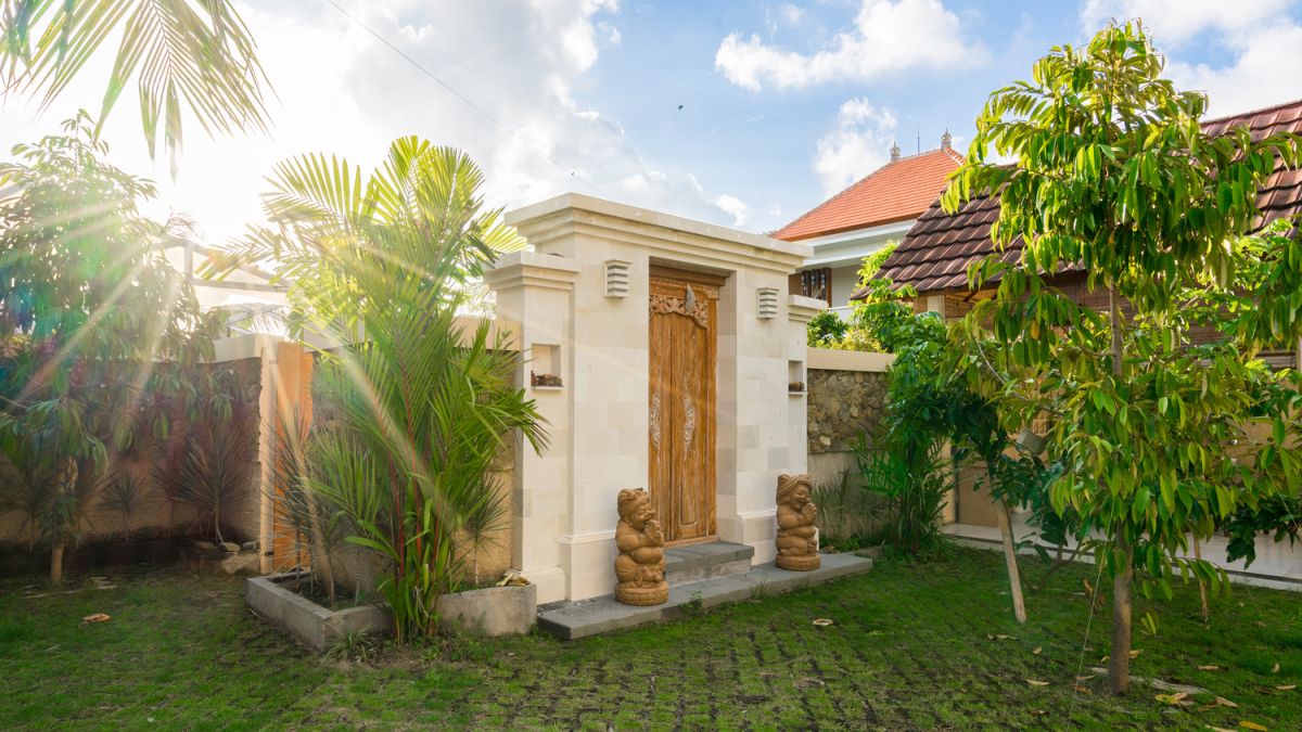 Serene Bali villa poolside patio with wooden dining set under blue umbrella, surrounded by tropical plants and traditional architecture. - Bali Villas