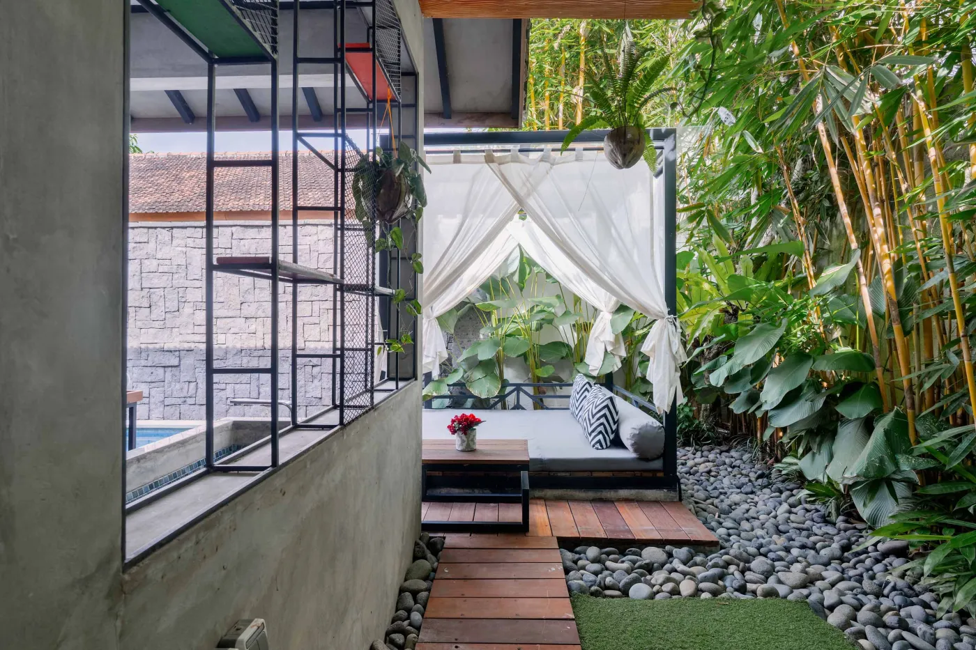 Rustic tropical kitchen with wooden cabinets, shelves of jars, tiled sink, and lush green plant wall behind metal frame, plus wooden dining bench and table. - Bali Villas
