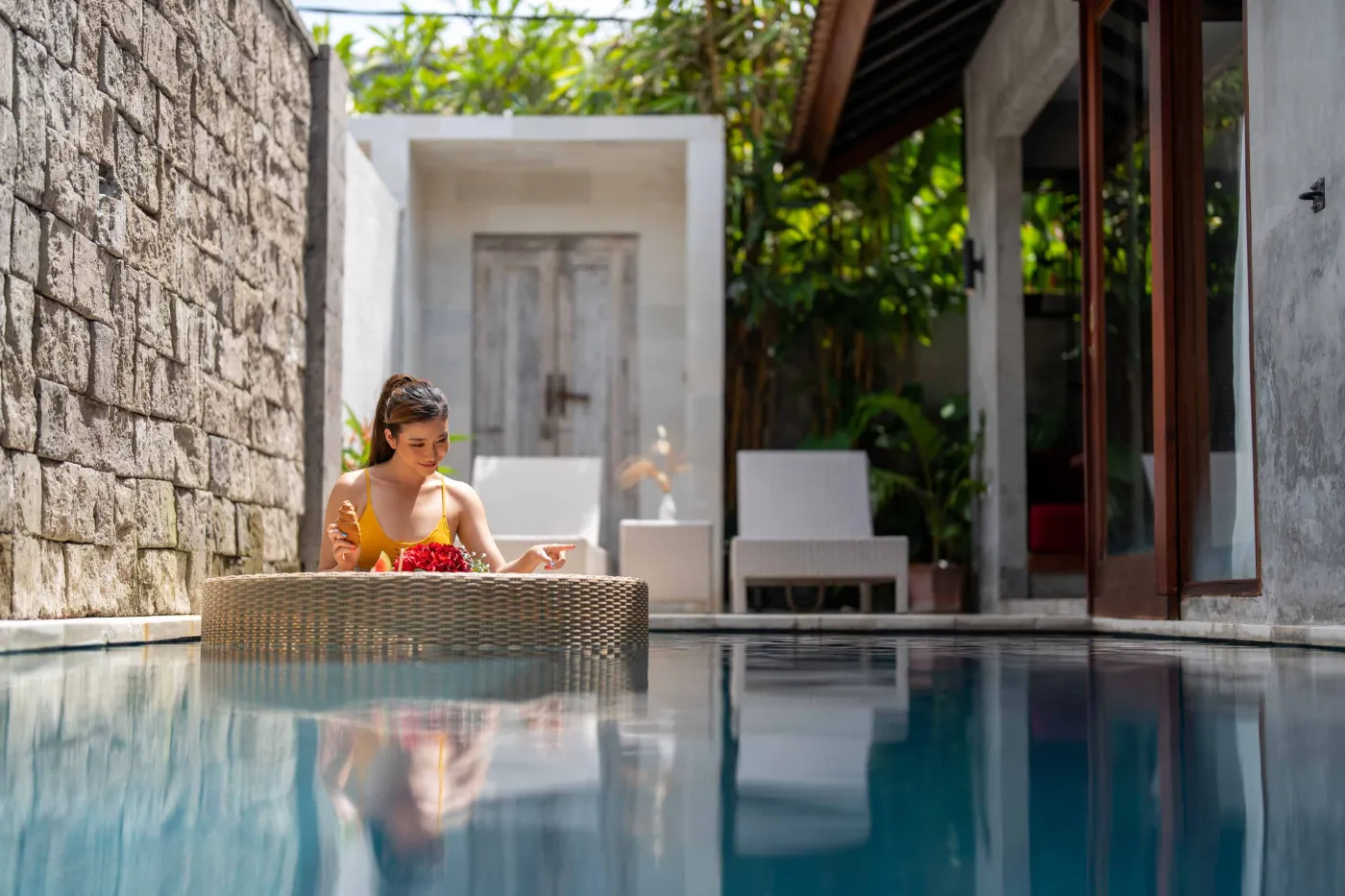 Rustic tropical kitchen with wooden cabinets, shelves of jars, tiled sink, and lush green plant wall behind metal frame, plus wooden dining bench and table. - Bali Villas