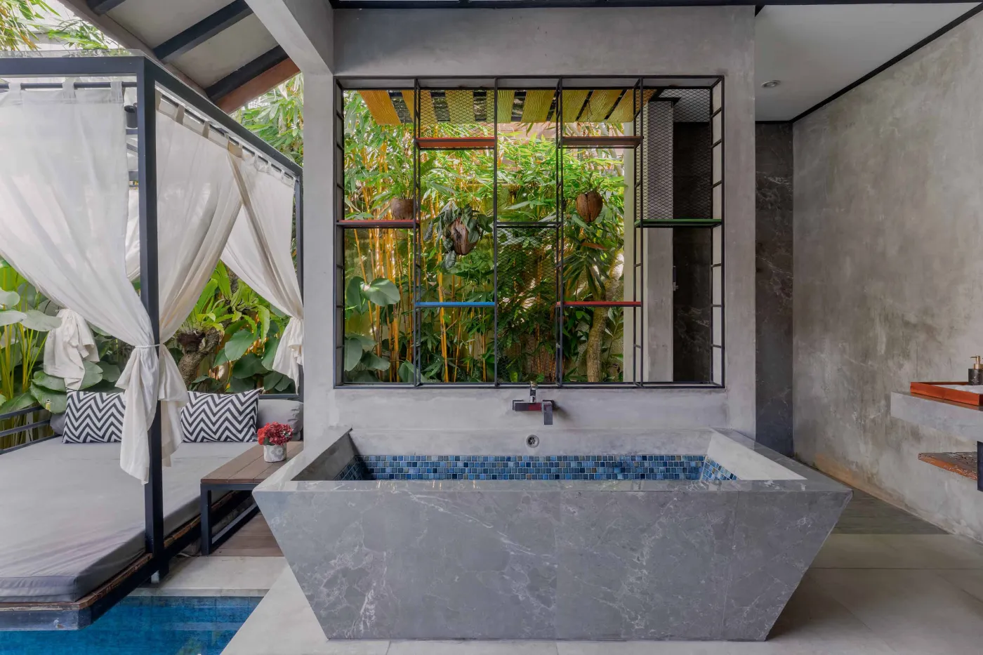 Rustic tropical kitchen with wooden cabinets, shelves of jars, tiled sink, and lush green plant wall behind metal frame, plus wooden dining bench and table. - Bali Villas