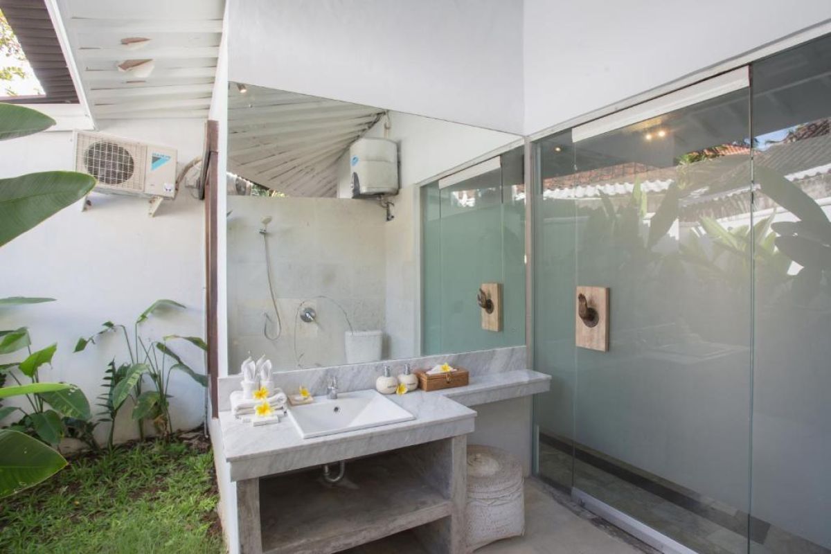 Spacious Balinese villa living area with rattan furniture, wooden accents, pendant lanterns, and open doors to a lush garden bedroom. - Bali Villas