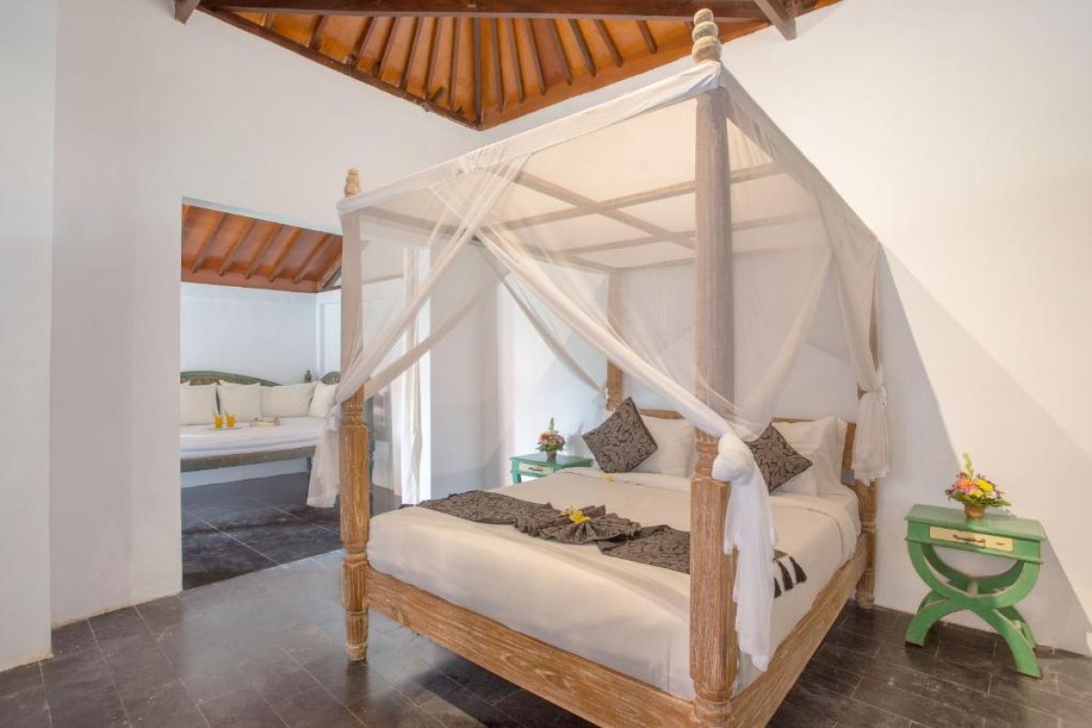 Spacious Balinese villa living area with rattan furniture, wooden accents, pendant lanterns, and open doors to a lush garden bedroom. - Bali Villas