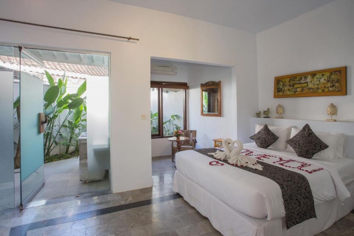 Spacious Balinese villa living area with rattan furniture, wooden accents, pendant lanterns, and open doors to a lush garden bedroom. - Bali Villas