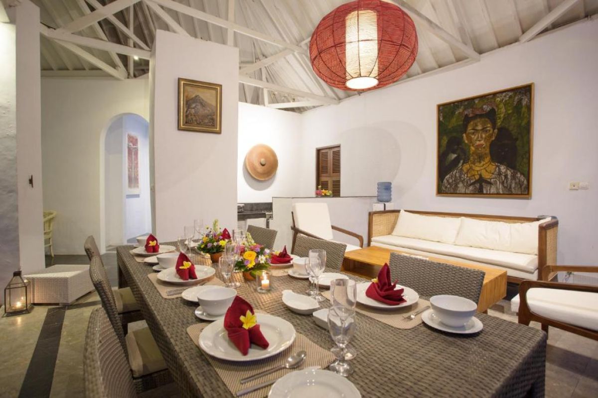 Spacious Balinese villa living area with rattan furniture, wooden accents, pendant lanterns, and open doors to a lush garden bedroom. - Bali Villas