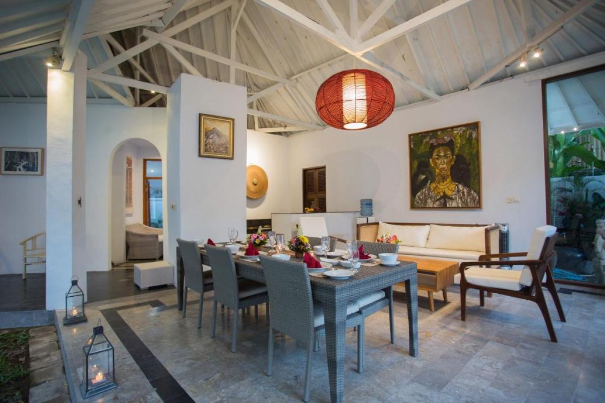 Spacious Balinese villa living area with rattan furniture, wooden accents, pendant lanterns, and open doors to a lush garden bedroom. - Bali Villas