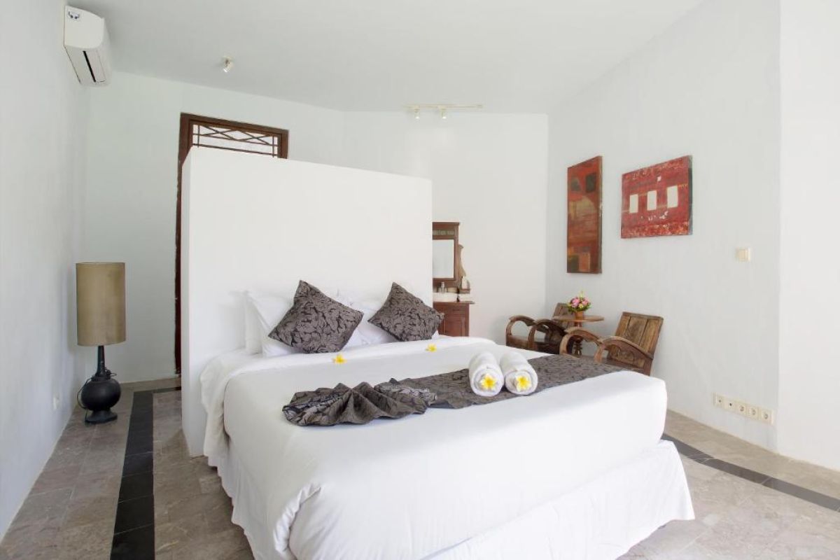 Spacious Balinese villa living area with rattan furniture, wooden accents, pendant lanterns, and open doors to a lush garden bedroom. - Bali Villas