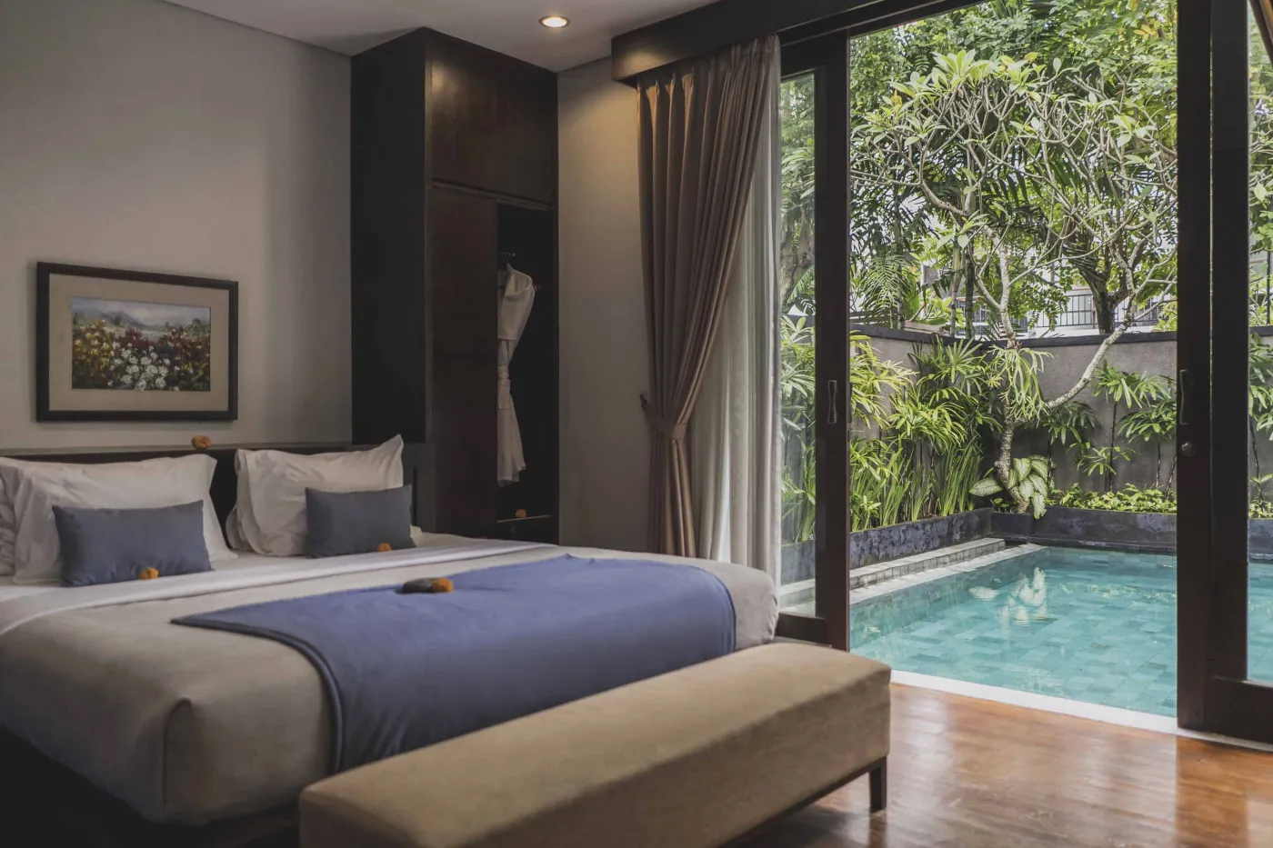 Luxury Bali villa bedroom with king bed, private infinity pool beyond sliding doors, wooden accents, and Netflix on TV. - Bali Villas