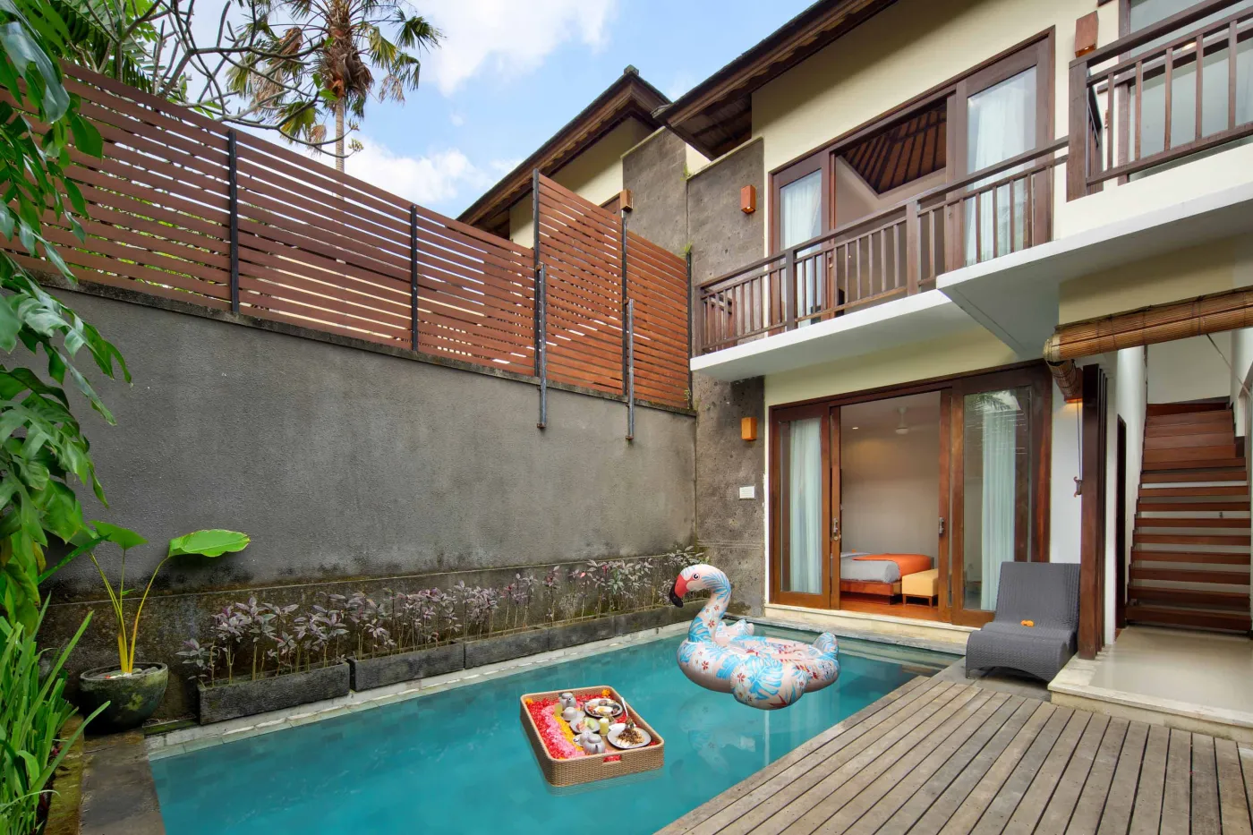 Luxury Bali villa bedroom with king bed, private infinity pool beyond sliding doors, wooden accents, and Netflix on TV. - Bali Villas