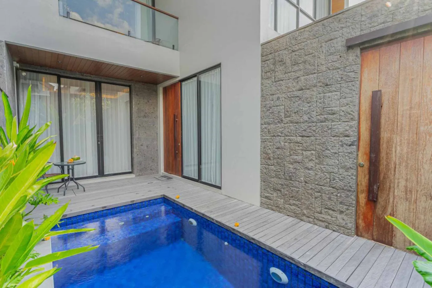 Modern tropical villa with private blue infinity pool, wooden deck, lush greenery, and glass balcony. - Bali Villas