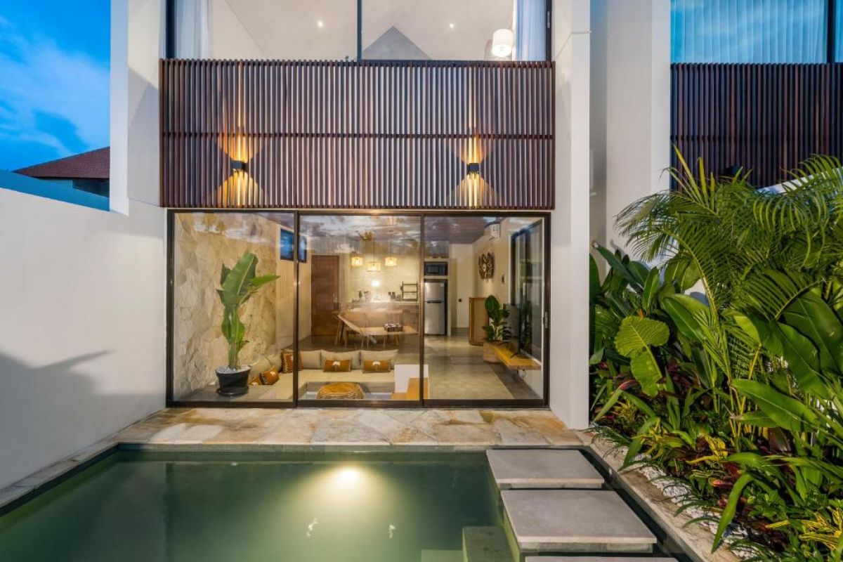 Modern tropical villa with open-plan living space, plunge pool, and lush greenery at dusk. - Bali Villas