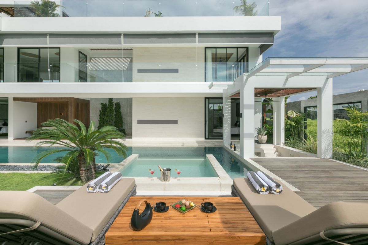 Modern tropical villa with infinity pool, outdoor lounge chairs, and coffee service overlooking lush greenery and rice fields. - Bali Villas