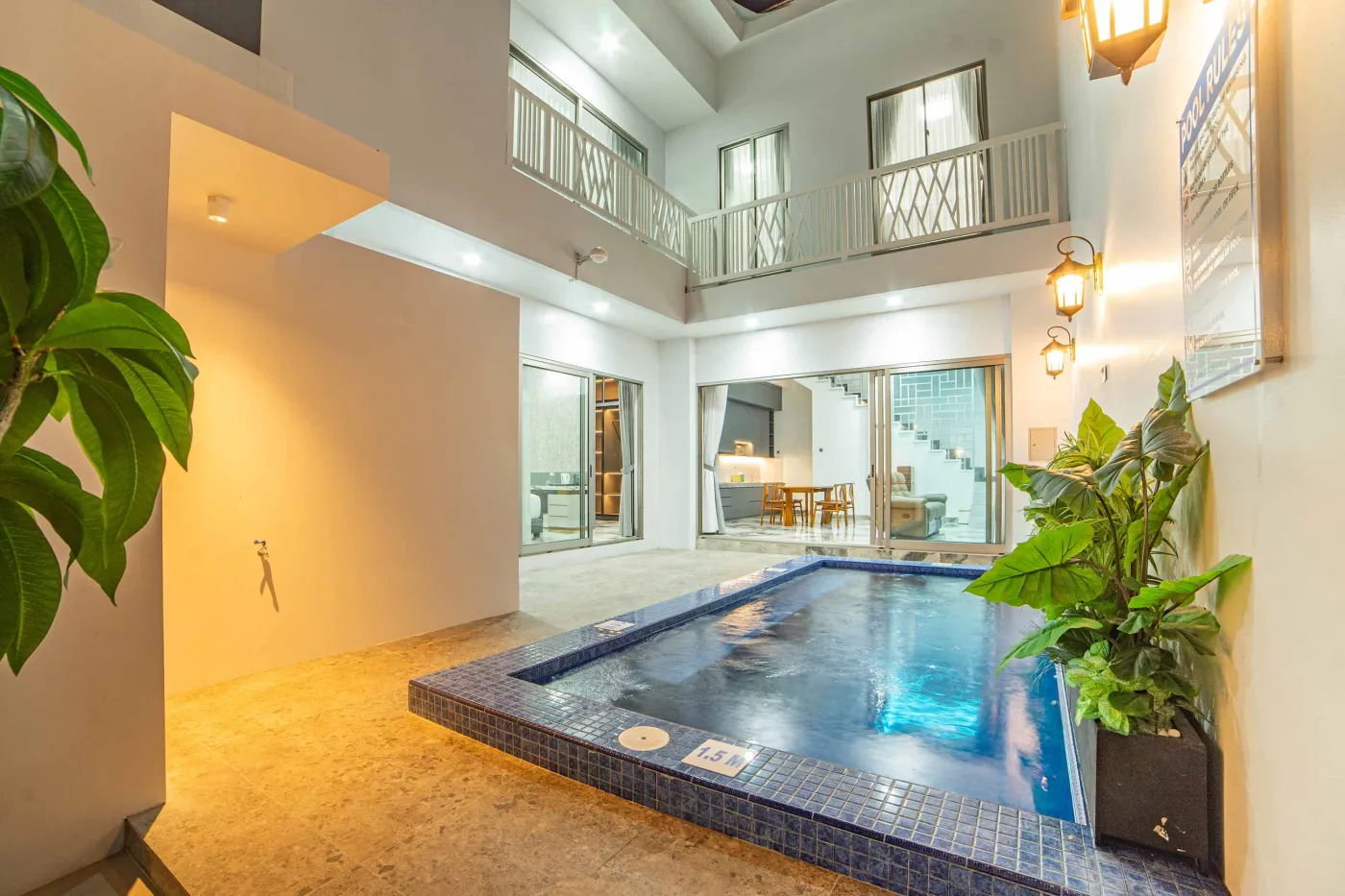 Modern indoor pool in a luxurious open-plan home with white walls, glass balcony, potted plants, and warm lighting. - Bali Villas