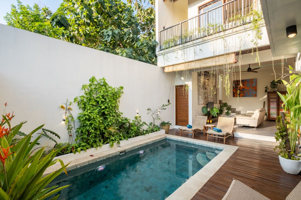 Serene modern tropical courtyard villa with turquoise lap pool, wooden deck lounge chairs, lush greenery, and open-air seating area. - Bali Villas