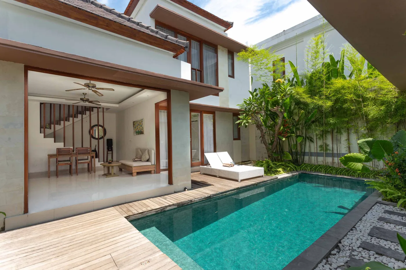 Modern tropical villa with private infinity pool, wooden deck, white lounge chairs, and lush green garden. - Bali Villas