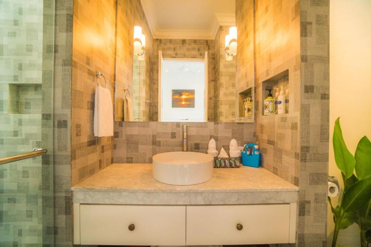 Modern gray-tiled bathroom featuring a white sink vanity, mirror, toilet, potted plants, and decorative window. - Bali Villas