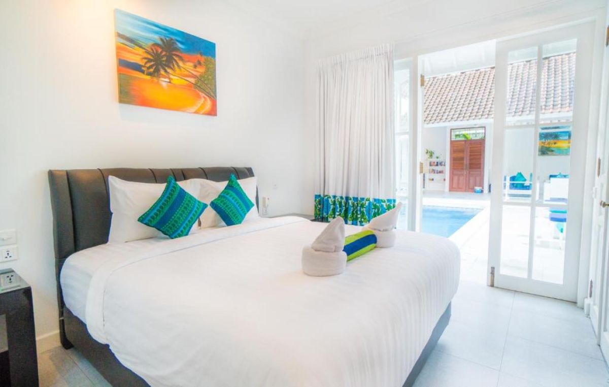 Modern gray-tiled bathroom featuring a white sink vanity, mirror, toilet, potted plants, and decorative window. - Bali Villas