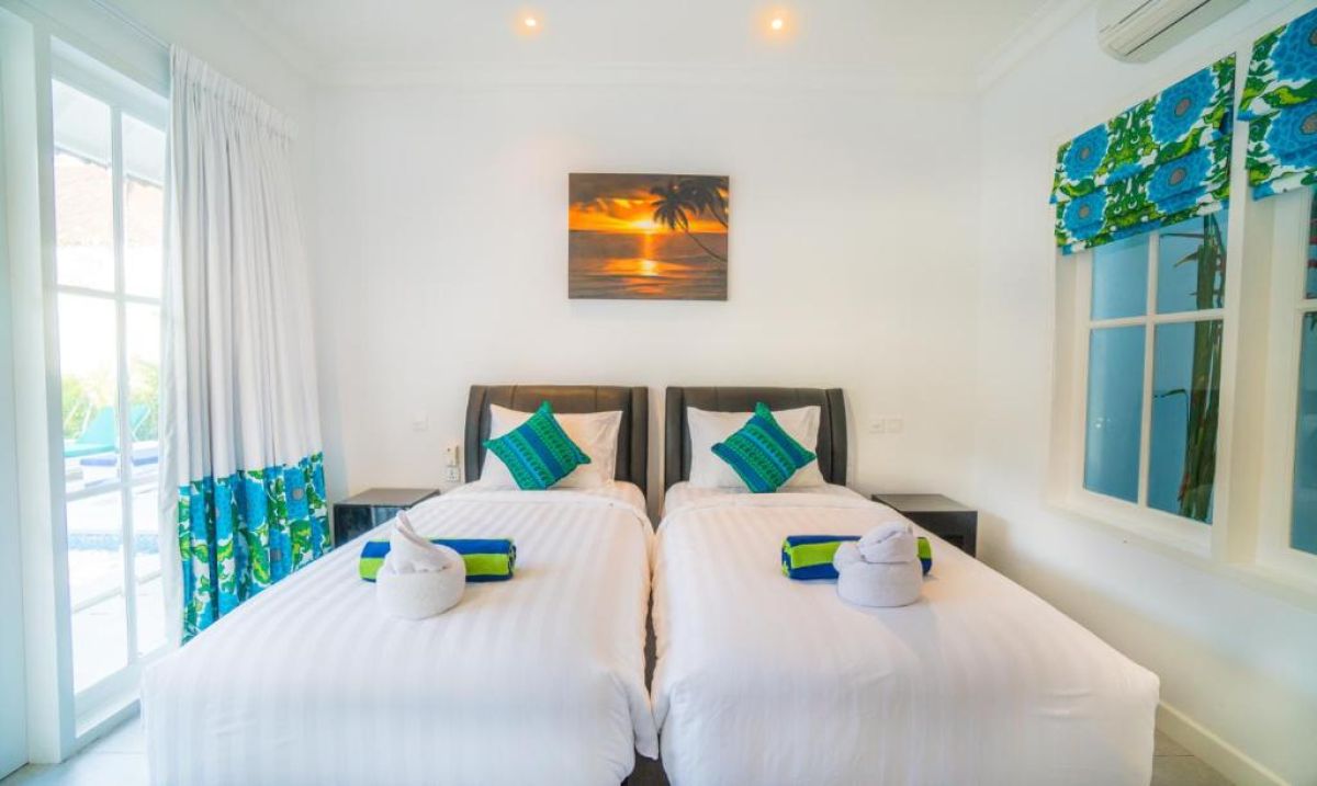 Modern gray-tiled bathroom featuring a white sink vanity, mirror, toilet, potted plants, and decorative window. - Bali Villas