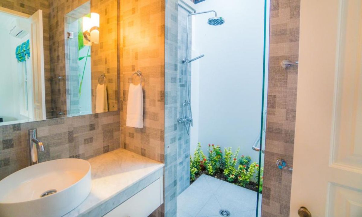 Modern gray-tiled bathroom featuring a white sink vanity, mirror, toilet, potted plants, and decorative window. - Bali Villas