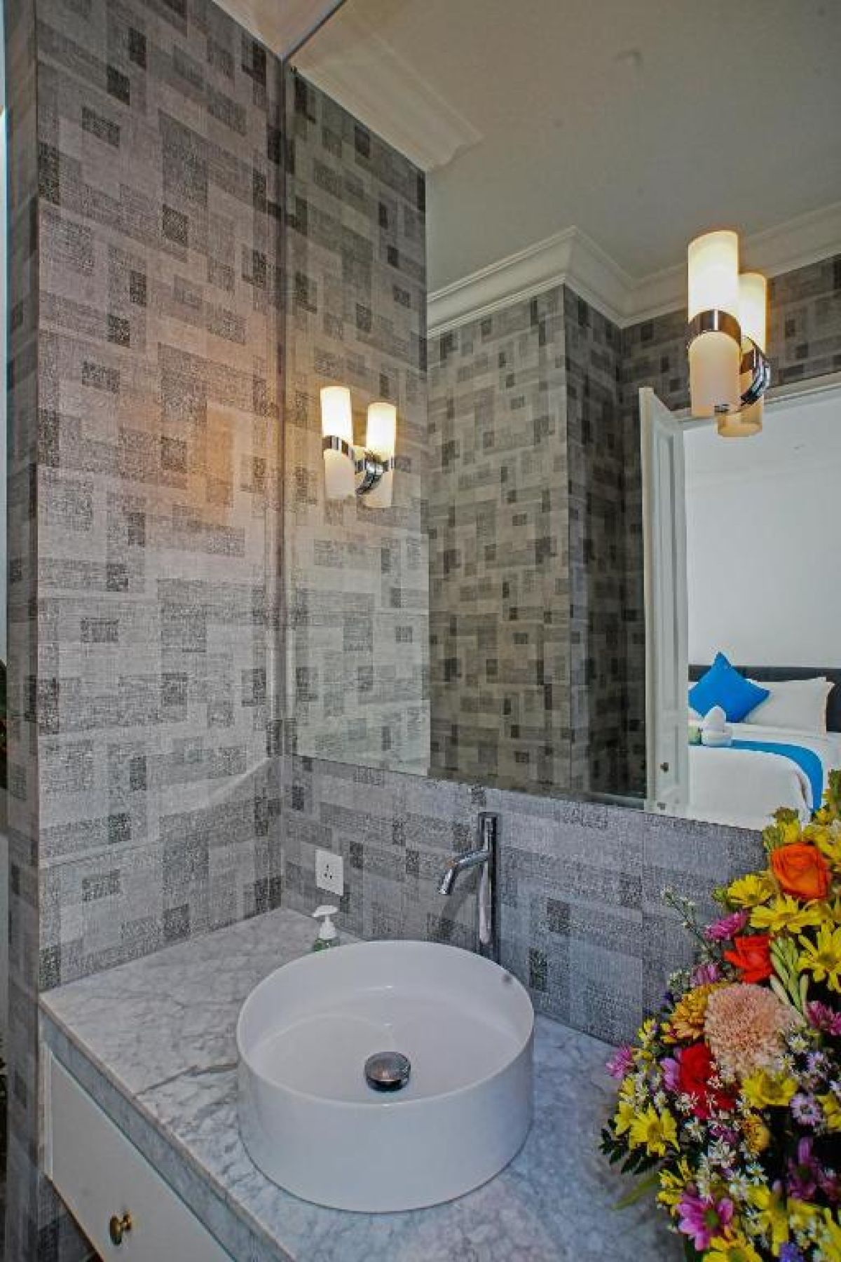 Modern gray-tiled bathroom featuring a white sink vanity, mirror, toilet, potted plants, and decorative window. - Bali Villas