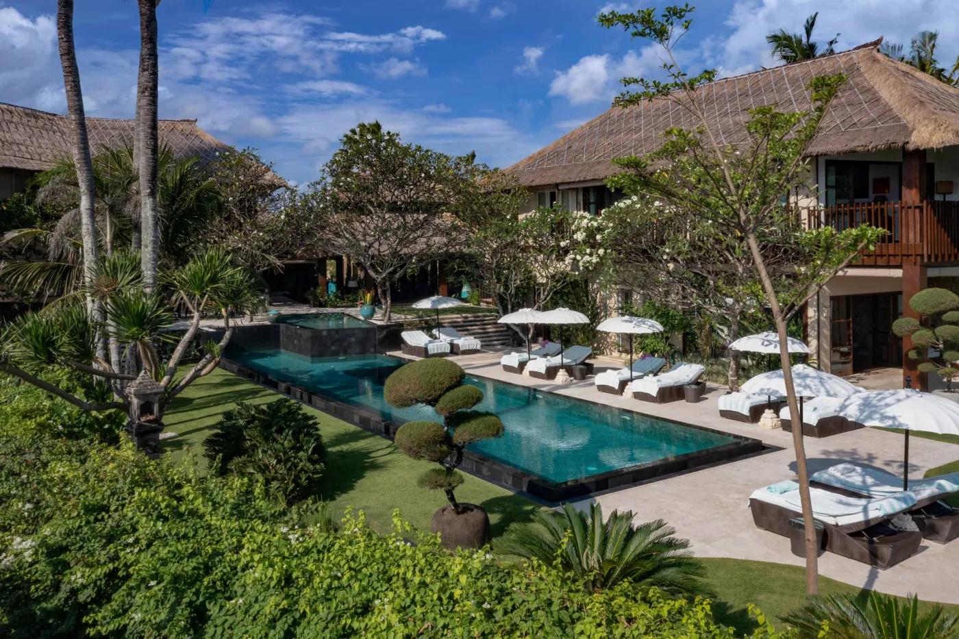 Luxurious infinity pool at a Balinese resort, surrounded by tropical palms, white loungers, and thatched-roof villas. - Bali Villas