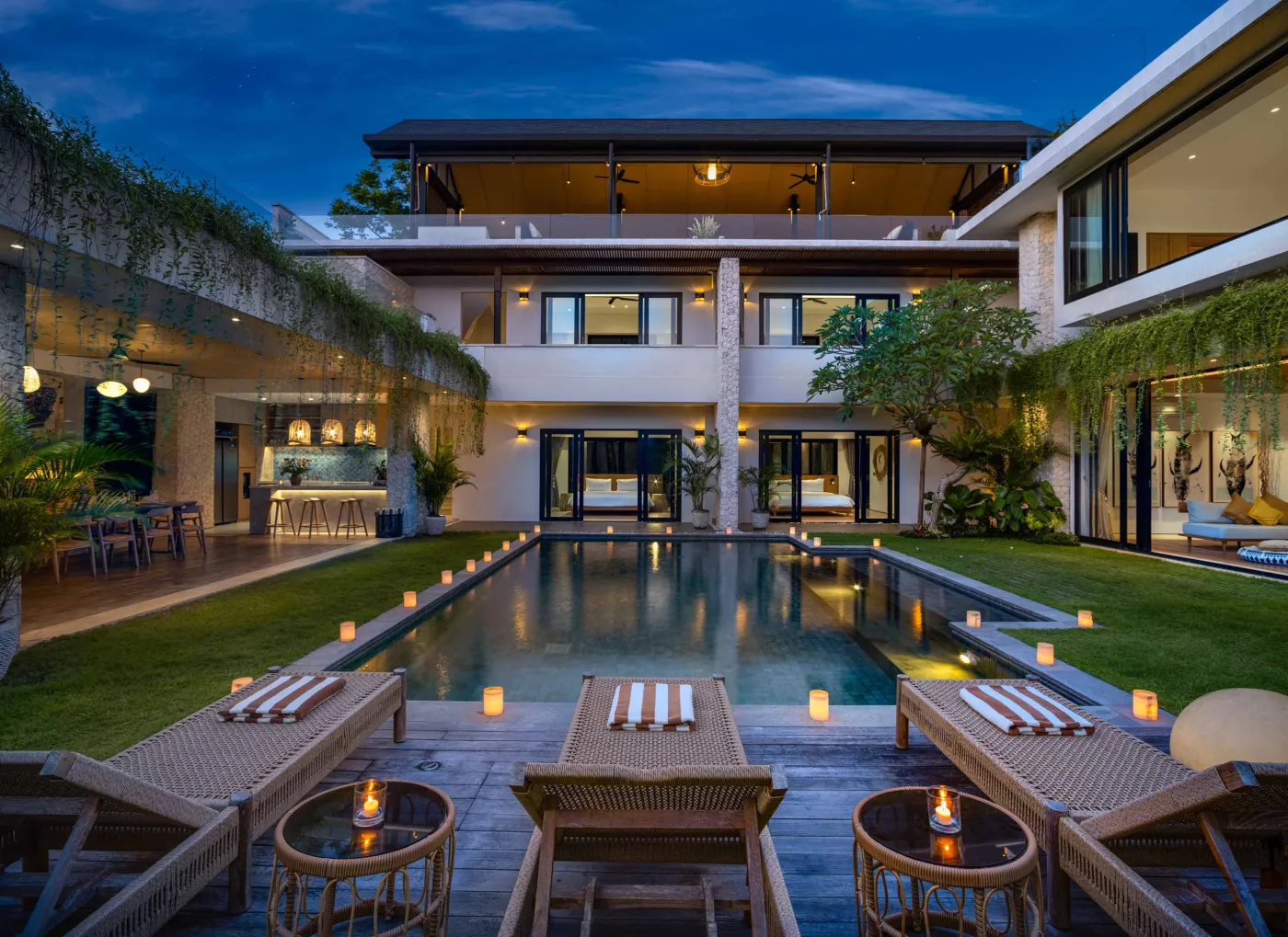 Luxurious tropical villa with infinity pool, rattan lounge chairs, and lush gardens at dusk. - Bali Villas